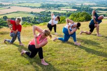 Groupe de femmes et d'hommes prenant part à des cours de yoga en plein air sur une colline . — Photo de stock