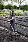 Woman raking freshly laid bed of soil in vegetable garden. — Stock Photo