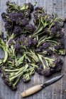 High angle close-up of purple sprouting broccoli and knife with wooden handle. — Stock Photo