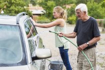 Senior Opa und Teenager-Enkelin waschen gemeinsam Auto in Einfahrt — Stockfoto