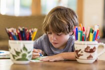 Маленький хлопчик малює різнокольоровими ручками за столом — стокове фото