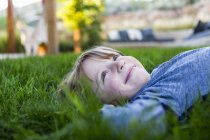 Portrait of smiling elementary age boy lying down in green grass — Stock Photo