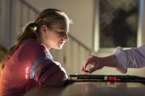 Teenager-Mädchen spielt Brettspiel mit unkenntlich gemachter Frau im Wohnzimmer bei Sonnenuntergang — Stockfoto
