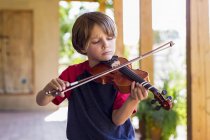 Elementary age boy playing violin outside in garden — Stock Photo