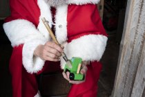 Gros plan de l'homme portant le costume du Père Noël tenant et brossant voiture jouet en bois
. — Photo de stock