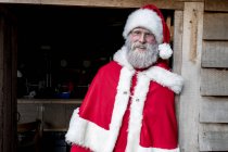 Man wearing Santa Claus costume standing in workshop doorway, looking in camera. — Stock Photo