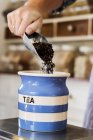 Close-up of person standing in a kitchen, placing loose tea into striped blue ceramic jar. — Stock Photo