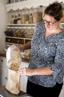 Woman standing in kitchen, pouring oats into paper bag. — Stock Photo