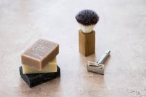 High angle close-up of stacked homemade bars of soap, shaving brush and razor. — Stock Photo