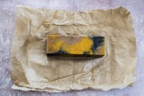 High angle close-up of yellow and black homemade bar of soap on brown paper. — Stock Photo