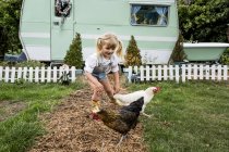 Blondes Mädchen mit Hühnern auf Gartenweg von weiß-grünem Retro-Wohnwagen. — Stockfoto