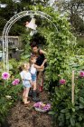 Femme et les filles debout sous l'arche dans le jardin, cueillette de haricots verts . — Photo de stock