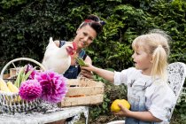 Frau und Mädchen sitzen am Tisch im Garten und füttern weiße Hühner. — Stockfoto