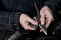 Alto ângulo close-up de mãos de pessoa que trabalha em faca artesanal usando pedaço de lixa . — Fotografia de Stock