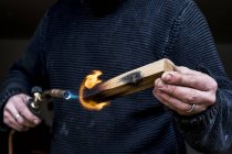 Close-up de homem segurando maçarico, carbonizando punho de madeira de uma faca . — Fotografia de Stock