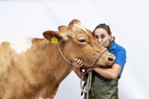 Retrato de agricultor feminino vestindo avental verde olhando na câmera e beijando vaca Guernsey . — Fotografia de Stock