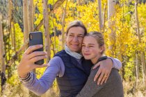 Portrait of mother and teen daughter taking selfie with autumn aspens in woods — Stock Photo
