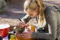 Дівчина-підліток різьблення великого гарбуза на Хеллоуїн . — стокове фото