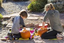 Teenage girl and elementary age boy carving pumpkins at Halloween. — Stock Photo