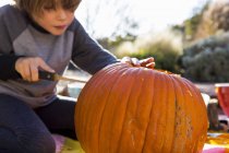 Menino da idade elementar esculpindo abóbora ao ar livre no Halloween . — Fotografia de Stock