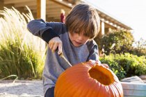 Elementary age boy carving pumpkin outdoors at Halloween. — Stock Photo