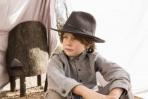 Elementary age boy wearing hat sitting in outdoor tent made of sheets — Stock Photo