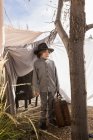 Junge im Grundschulalter trägt Hut mit Gepäck in Outdoor-Zelt aus Laken — Stockfoto