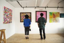Visão traseira de homem e mulher olhando pinturas abstratas em uma galeria de arte . — Fotografia de Stock