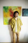 Homem japonês de chapéu em pé na frente de pinturas abstratas em uma galeria de arte . — Fotografia de Stock