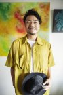 Japaner steht vor abstrakten Gemälden in einer Kunstgalerie und lächelt in die Kamera. — Stockfoto