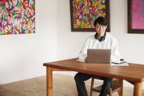 Uomo giapponese seduto a un tavolo in una galleria d'arte, guardando computer portatile . — Foto stock
