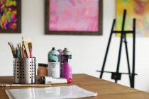 Interior view of art gallery with studio space, easel and cans of spray paint on a table. — Stock Photo