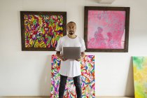 Японский мужчина, стоящий в художественной галерее, держащий ноутбук, смотрящий в камеру . — стоковое фото