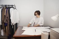 Mujer japonesa en gafas trabajando en un escritorio en una pequeña boutique de moda
. - foto de stock