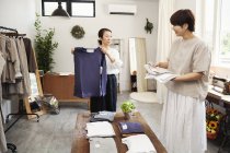 Две японки стоят в маленьком модном бутике, расставляя футболки на кофейном столике . — стоковое фото