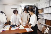 Trois Japonaises debout à une table dans une petite boutique de mode, regardant des échantillons de tissu . — Photo de stock