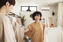 Two Japanese women standing in a small fashion boutique, looking at tops. — Stock Photo