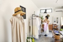 Mujer japonesa de pie en una boutique, mirando la ropa en una barandilla . - foto de stock