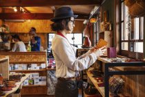 Japanese woman wearing hat and glasses browsing merchandise in a leather shop. — Stock Photo