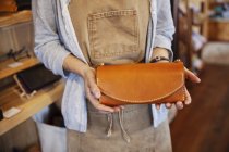Close-up of woman standing in a leather shop, holding leather clutch bag. — Stock Photo