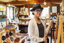 Mujer japonesa con sombrero y gafas de pie en una tienda de cuero, con cinturón de cuero
. - foto de stock