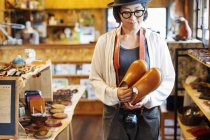 Mujer japonesa con sombrero y gafas de pie en una tienda de cuero, sosteniendo un par de zapatos de cuero
. - foto de stock