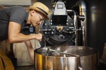Японский мужчина в шляпе и очках, стоящий в Эко-кафе, работающий кофе жаровня машина . — стоковое фото