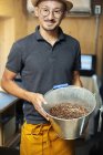 Japanese man standing in Eco Cafe, holding metal bucket with freshly roasted coffee beans, smiling in camera. — Stock Photo
