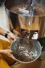 High angle close-up of person holding metal bucket with freshly roasted coffee beans. — Stock Photo