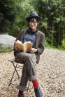 Donna giapponese con occhiali e cappello seduta sulla sedia fuori Eco Cafe, libro di lettura
. — Foto stock