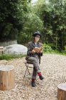 Japanerin mit Brille und Hut sitzt auf Stuhl vor Öko-Café und liest Buch. — Stockfoto