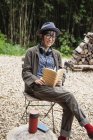 Японская женщина в очках и шляпе сидит на стуле возле Эко Кафе, читает книгу . — стоковое фото