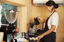 Japanese woman wearing apron standing in an Eco Cafe, preparing coffee. — Stock Photo