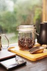 Close-up de cafeteira, jarra de vidro com grãos de café e pá de café de metal na placa de madeira . — Fotografia de Stock